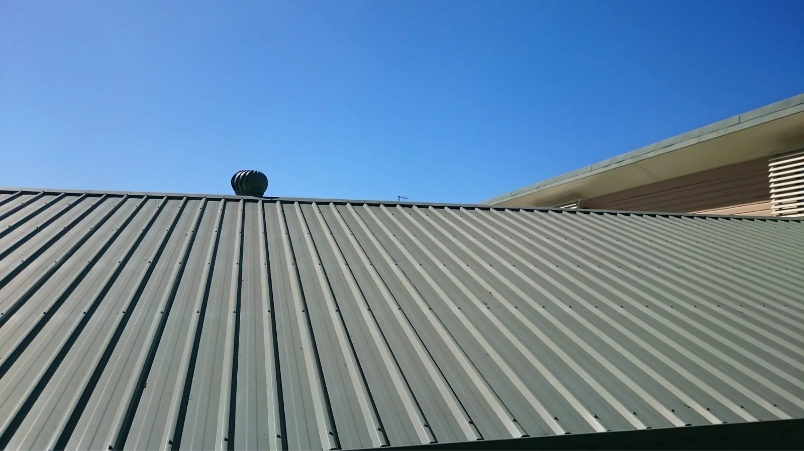 Corrugated metal roof with a turbine vent under clear blue sky